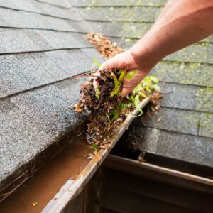 person scooping debris out of gutter